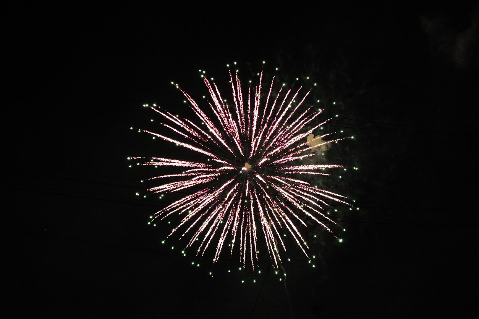 夜空にいくつもの花火が浮かび、静かな街を照らしている情景